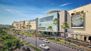 A modern shopping mall with a glass facade, palm trees, and a busy street. - HangoutSpacez Queensbay at Bayan Lepas Penang (Bayan Lepas)