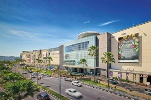 Un moderno centro commerciale con facciata in vetro curvo, palme e cielo azzurro.