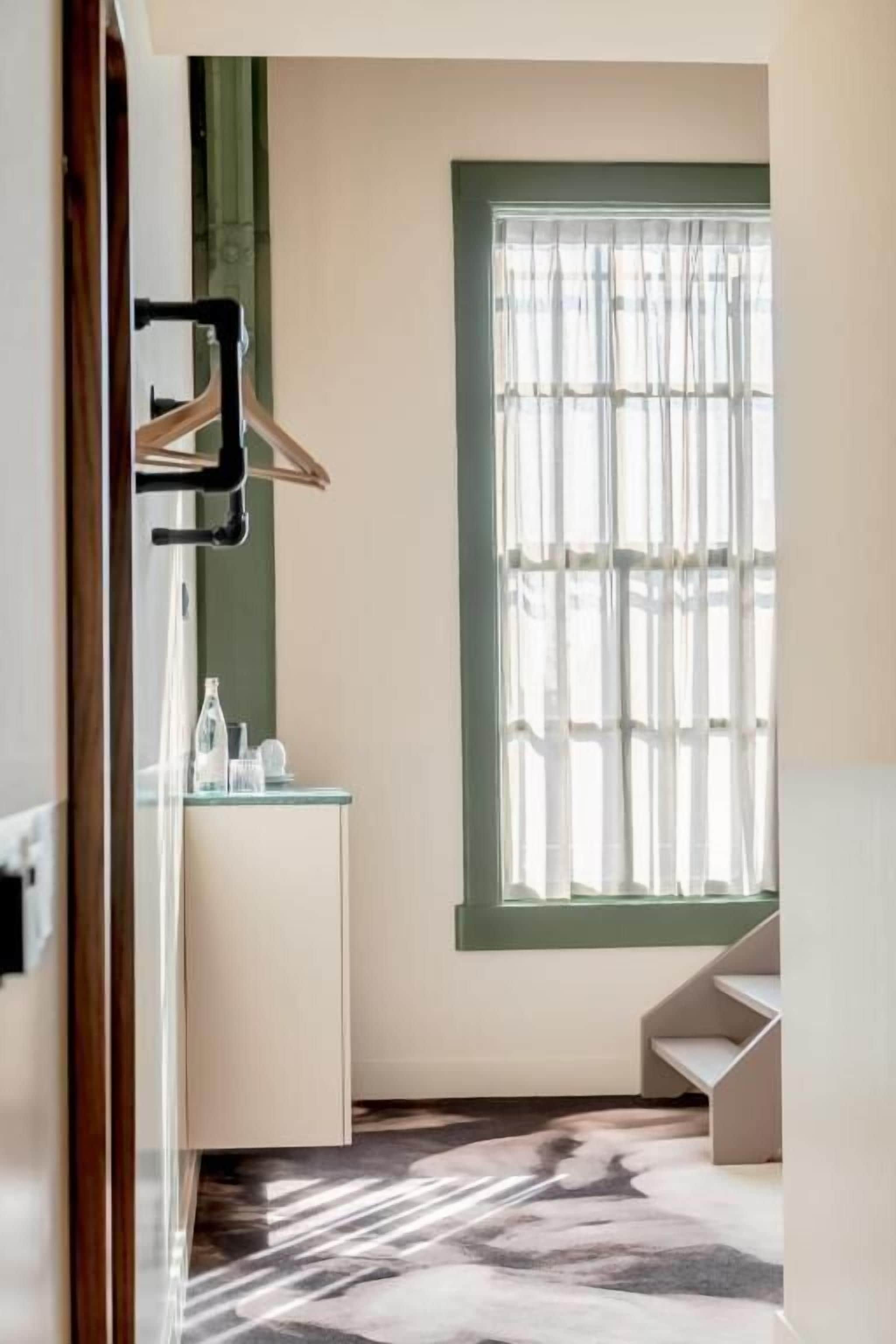 A modern bathroom with a mirror, a sink, and a window with sheer curtains.