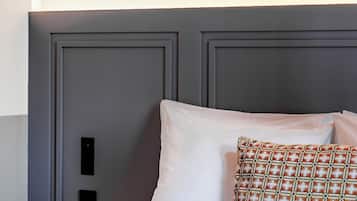 A neatly made bed with white and patterned pillows, a grey headboard, and two framed artworks on the wall.