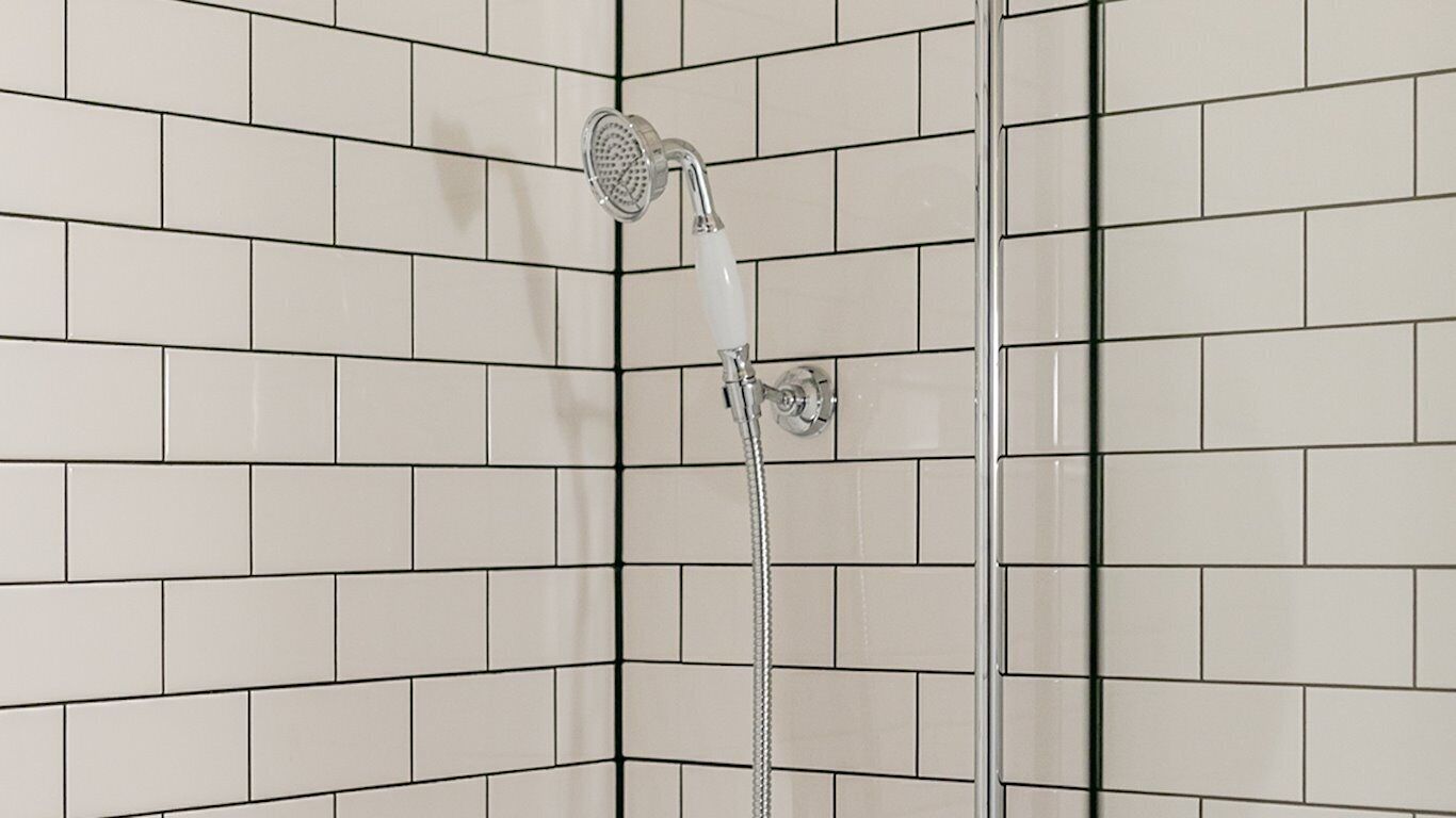 Een douche met een handdouche in een betegelde badkamer.
