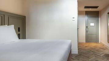 Une chambre d’hôtel avec un lit, une porte et un parquet à motifs en chevrons.