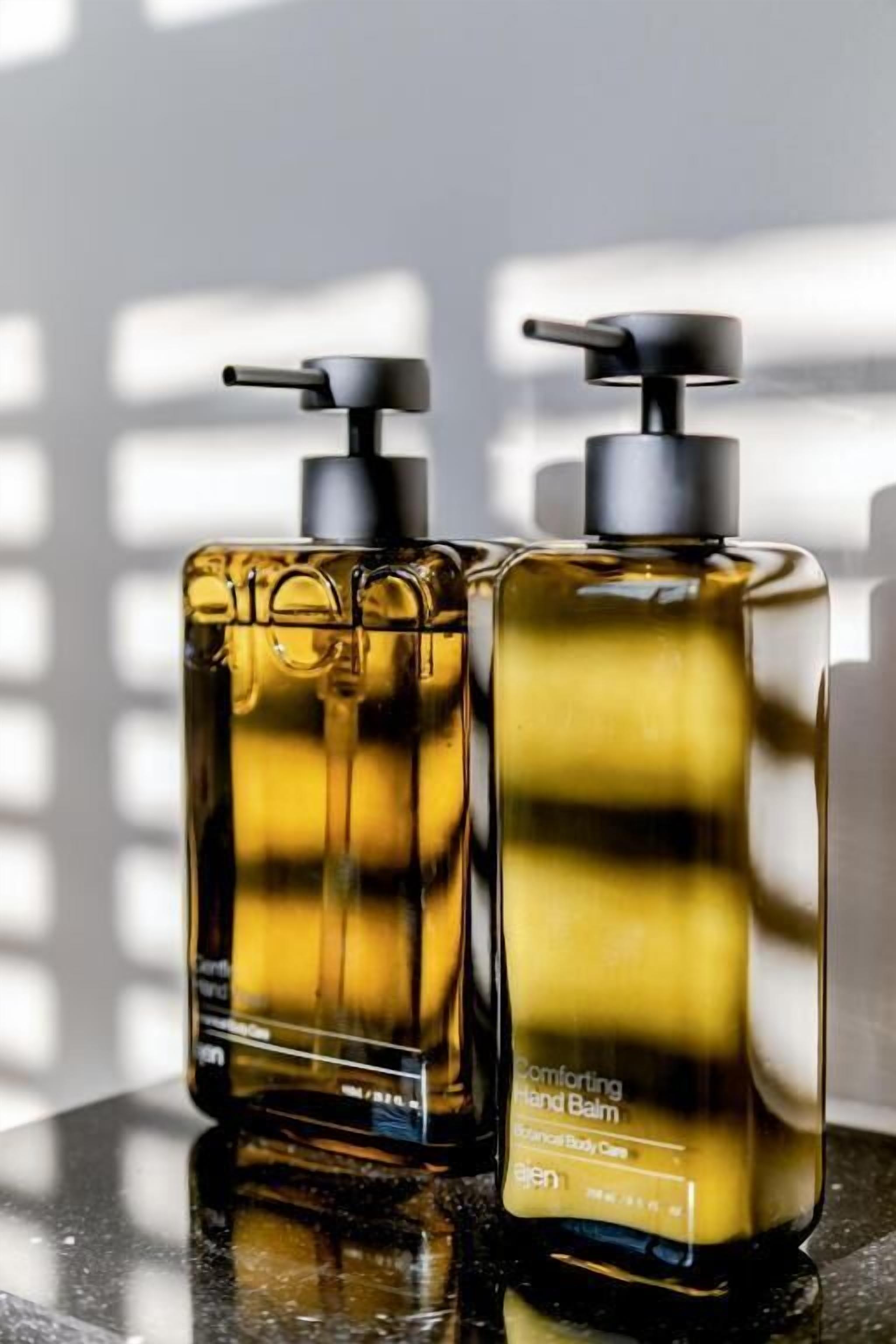 Two bottles of hand balm on a reflective surface.