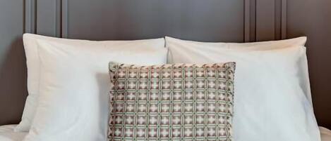 A neatly made bed with white and patterned pillows, a grey headboard, and three framed artworks on the wall above.