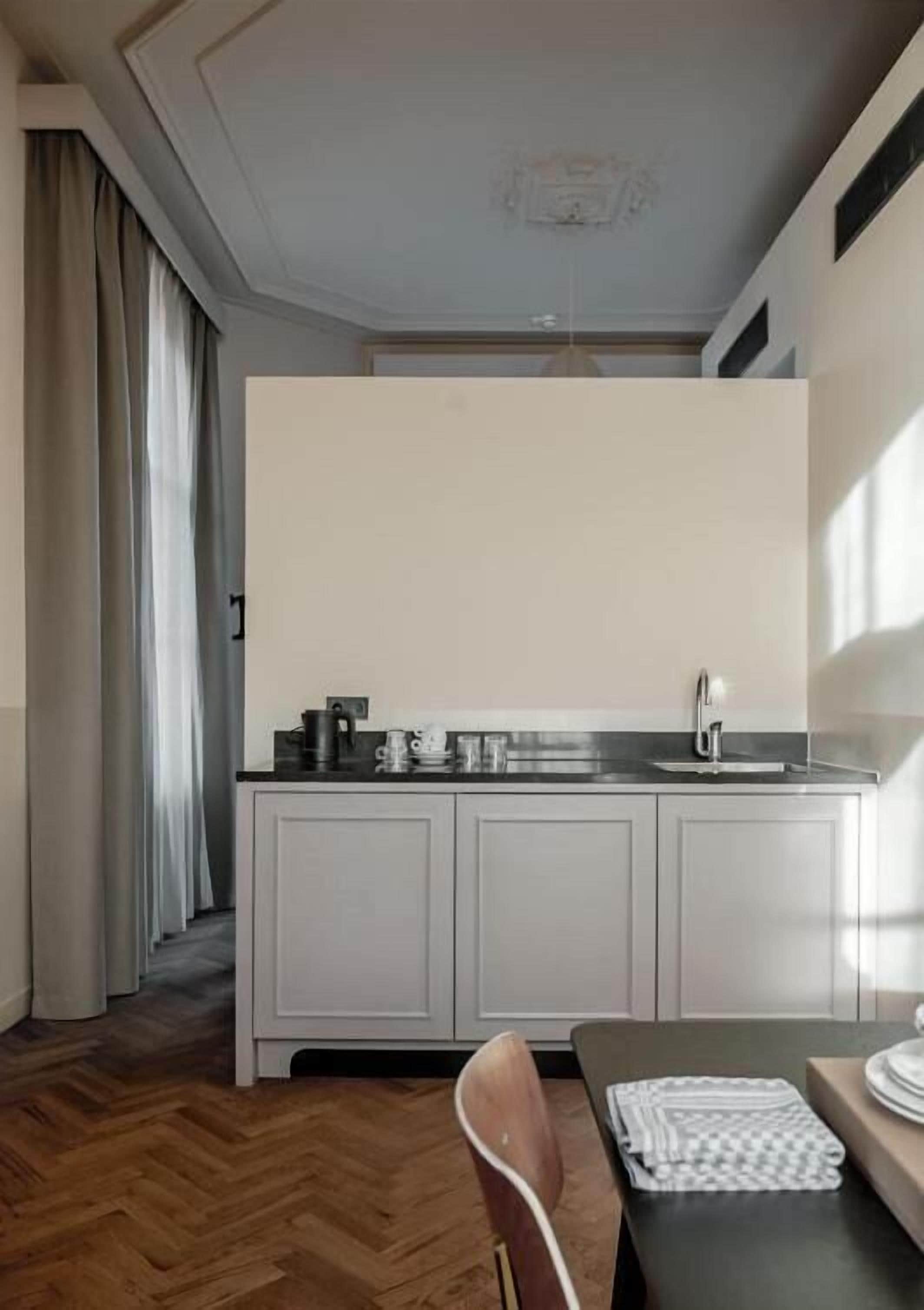 A modern kitchen with white cabinets, a black countertop, and a dining area with a wooden chair and a table.