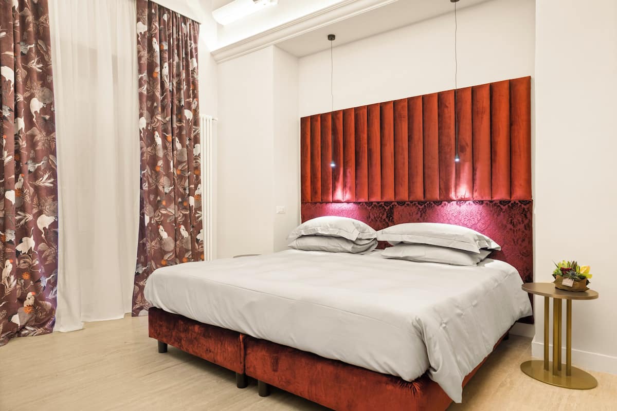 A modern bedroom with a large bed, a red headboard, and a small side table with a plant.