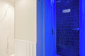 Ein Badezimmer mit Marmorwand, einem weißen Heizkörper und einer Dusche mit einer blau beleuchteten Glastür.