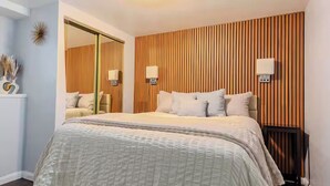 Un dormitorio con una cama grande, panel de pared de madera, dos lámparas de noche y un espejo.
