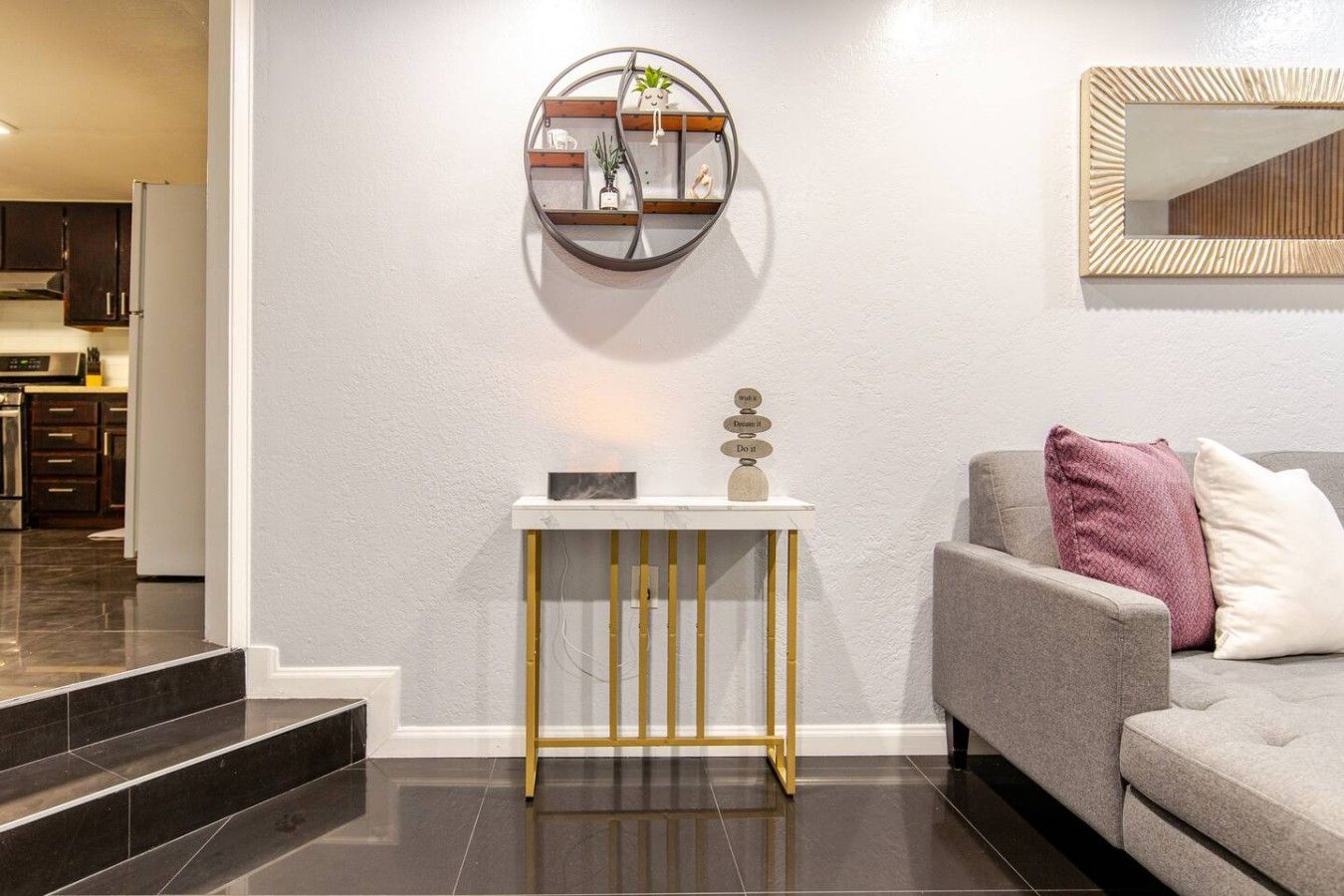 A modern living room with a grey sofa, a white console table with a decorative item, and a wall-mounted mirror.