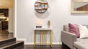 A modern living room with a grey sofa, a white console table with a decorative item, and a wall-mounted mirror.