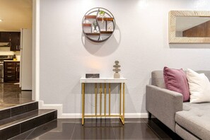 Una sala de estar moderna con un sofá gris, una consola blanca con un objeto decorativo y un espejo montado en la pared.