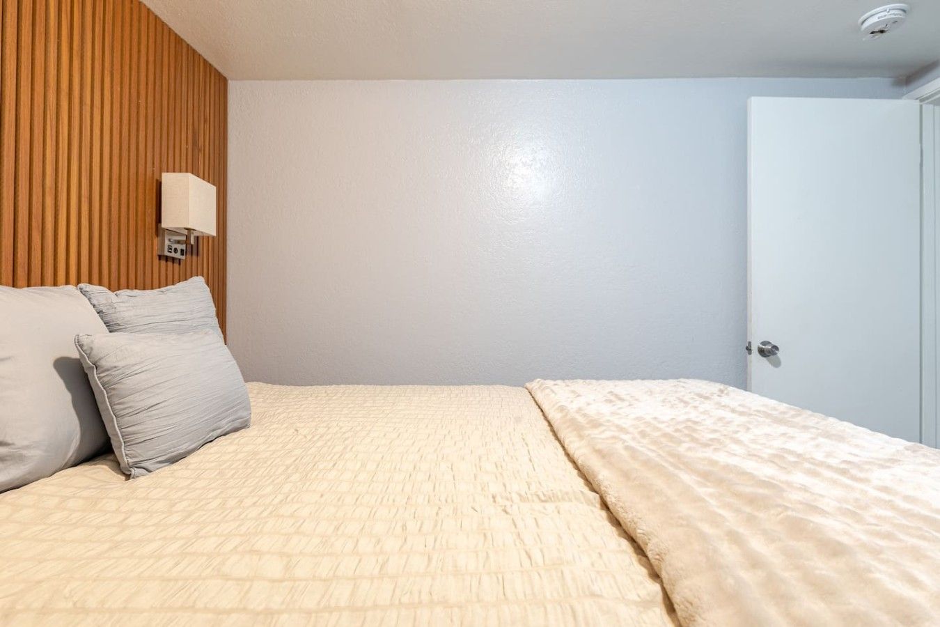 A bedroom with a bed, pillows, a wall-mounted light, and a door.