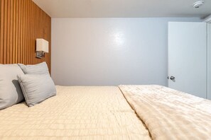 A bedroom with a bed, pillows, a wall-mounted light, and a door.