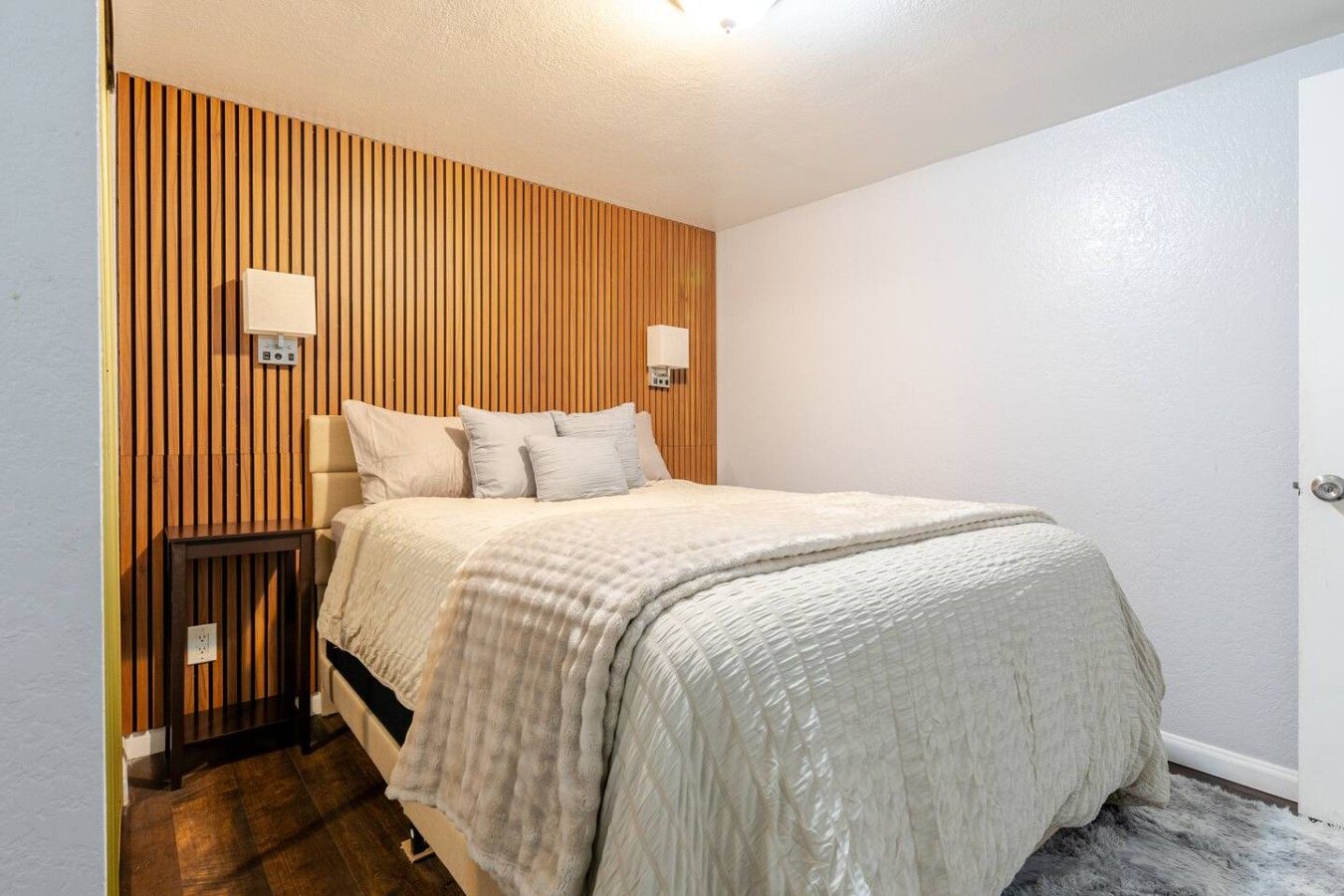 Un dormitorio con cama, mesitas de noche, un cabecero de listones de madera y una puerta.