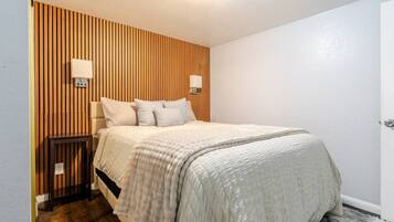 Un dormitorio con cama, mesitas de noche, un cabecero de listones de madera y una puerta.