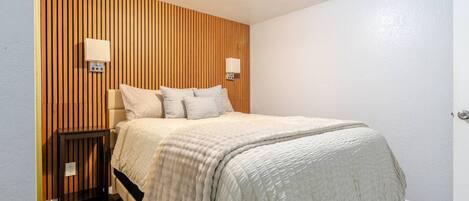Une chambre à coucher avec un lit, des tables de chevet, un mur recouvert de lambris en bois et une porte.