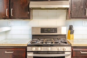 Una cocina con estufa de acero inoxidable, armarios de madera y un bloque de cuchillos en la encimera.