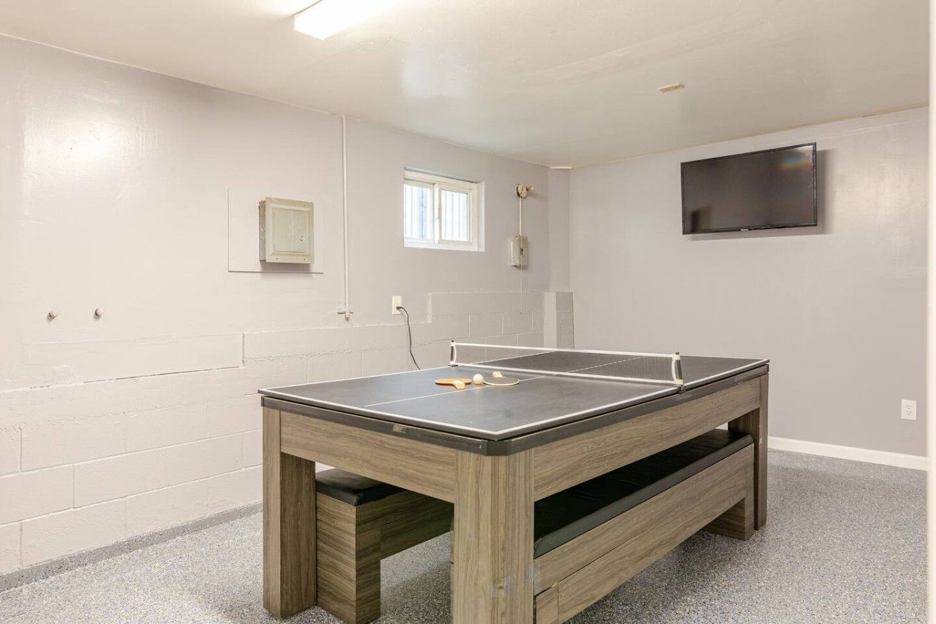 Una habitación con mesa de ping pong, televisor montado en la pared y ventana que proporciona luz natural.