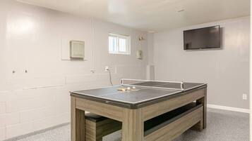 Una habitación con mesa de ping pong, televisor montado en la pared y ventana que proporciona luz natural.