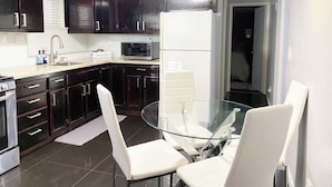 Una cocina moderna con armarios de madera oscura, un refrigerador blanco, un microondas y una mesa de comedor de vidrio con sillas blancas.