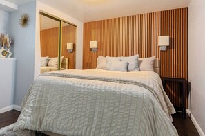 Un dormitorio con cama, lámparas de noche, un espejo y un panel de listones de madera.