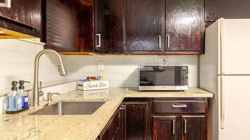 A kitchen with dark wooden cabinets, a white refrigerator, a stainless steel sink, and a microwave on the countertop.