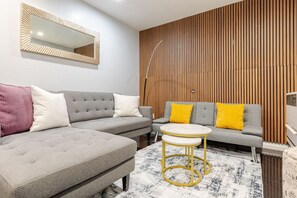 Una sala moderna con un sofá seccional gris, una mesa redonda de centro y una pared con listones de madera.
