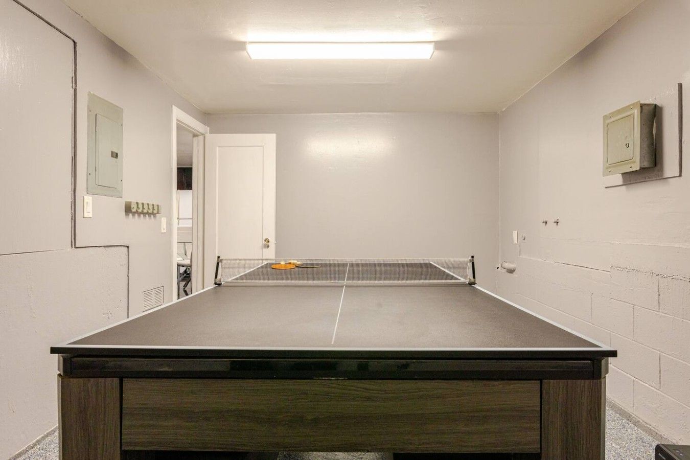 Ett rum med ett bordtennisbord, en dörr och en väggmonterad elcentral.