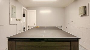 Quarto com mesa de pingue-pongue, uma porta e um quadro elétrico na parede.
