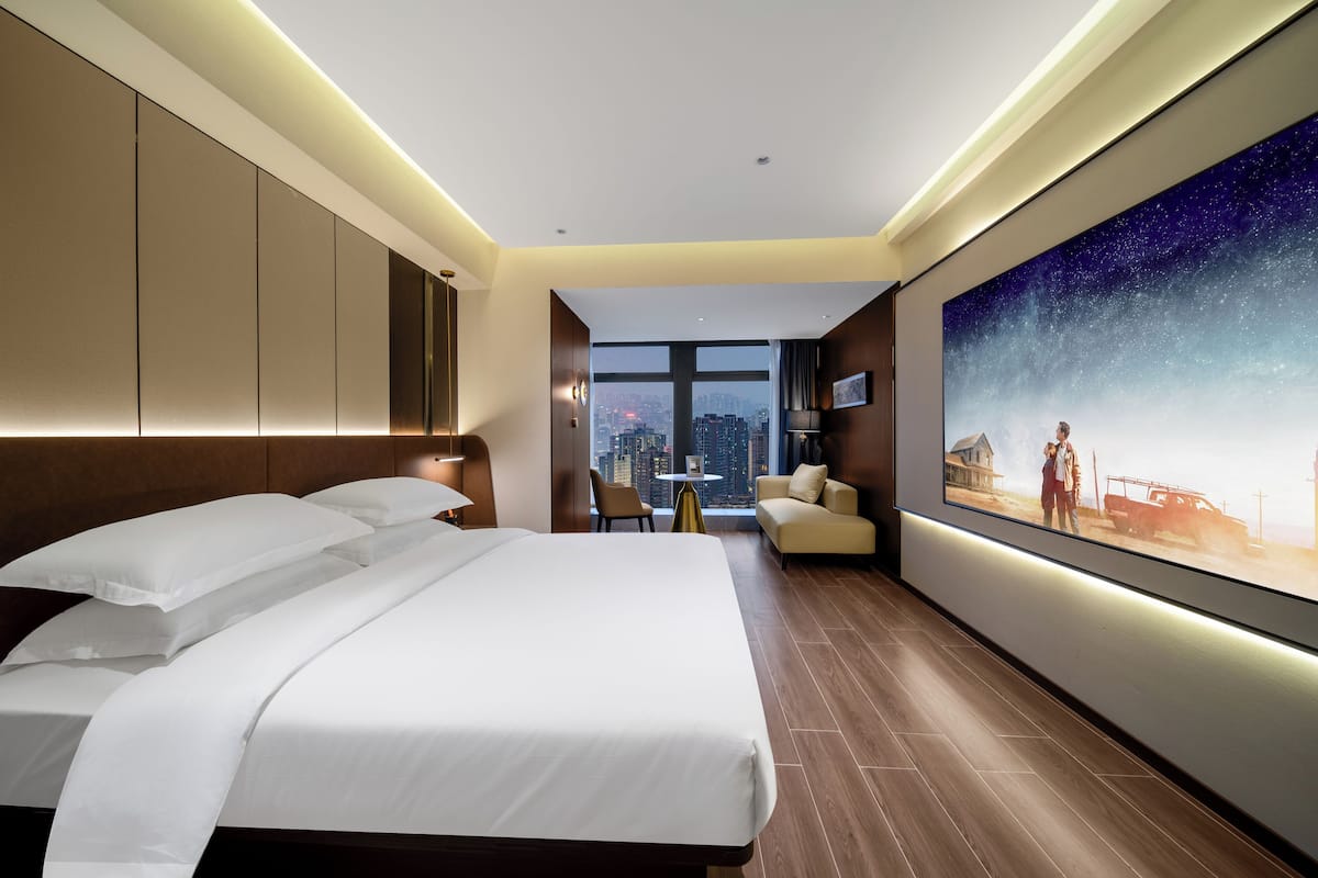 Une chambre d’hôtel moderne dotée d’un grand lit, d’une vue sur la ville, d’un canapé et d’un grand téléviseur fixé au mur.