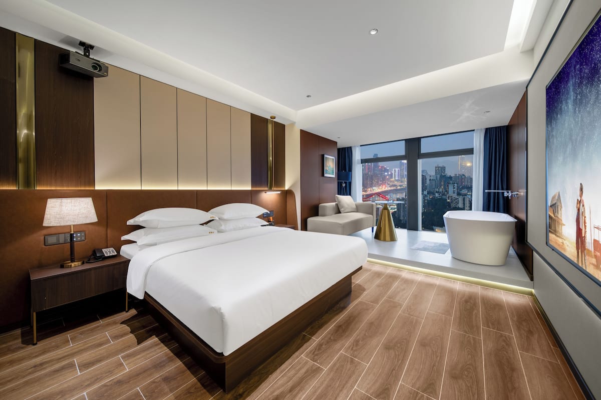 Une chambre d’hôtel moderne, dotée d’un grand lit, d’un bureau, d’une chaise et offrant une vue sur le paysage urbain.