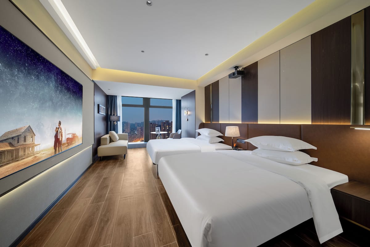 Une chambre d’hôtel avec deux lits, un bureau, une chaise et une grande fenêtre donnant sur la ville.