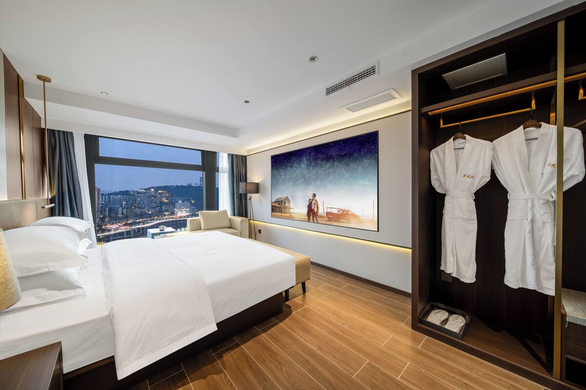 Une chambre d’hôtel avec un grand lit, une vue sur la ville, un tableau au mur et un porte-peignoir avec des peignoirs.