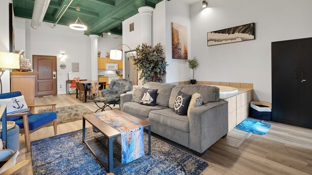 Una sala de estar moderna con un sofá gris, un sillón azul y una mesa de centro con una alfombra de temática náutica.