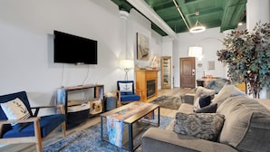 Una sala de estar con televisor de pantalla plana, muebles azul grisáceos, chimenea y una planta grande.