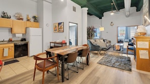 Una cocina amplia con gabinetes de madera, un comedor con una mesa larga y sillas, y una sala de estar con sofá y mesa de centro.
