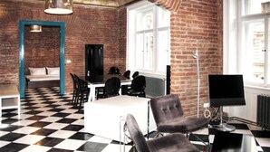 A room with a checkered floor, brick walls, a sofa, a table, chairs, a TV, and a radiator.