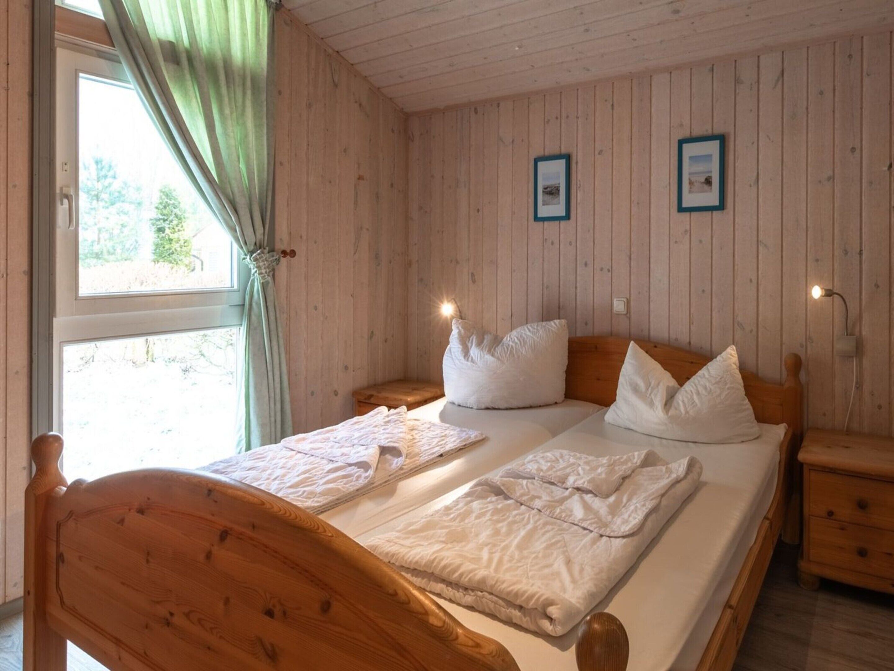 A wooden-paneled bedroom with a bed, two bedside tables, and a window with curtains.