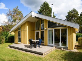 Une maison moderne avec une façade en bois, de grandes portes-fenêtres coulissantes et une terrasse aménagée avec du mobilier d’extérieur.