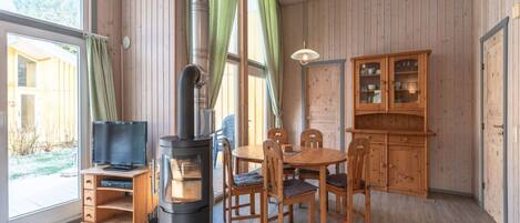 A cozy room with a wood-burning stove, wooden furniture, and large windows.
