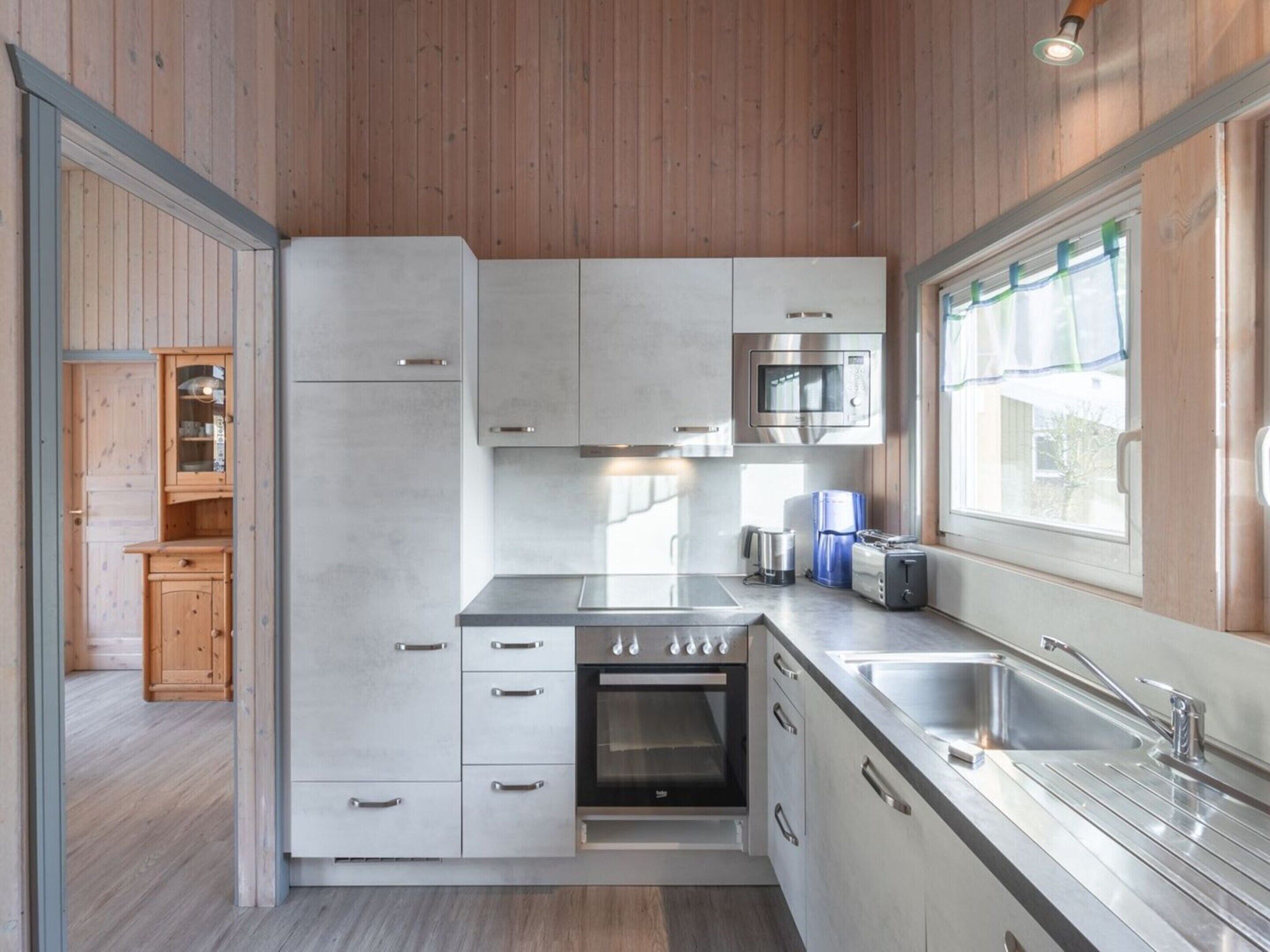 A modern kitchen with stainless steel appliances, wooden cabinets, and a large window providing natural light.
