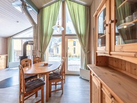 Um interior em madeira com uma mesa de jantar, cadeiras e uma grande janela com cortinas.