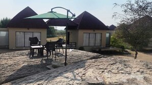 A modern building with a patio area featuring outdoor seating and a green umbrella. - Jawai Zinc Journey by The Fern (Bali)