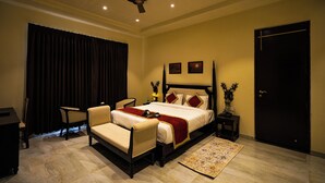 A hotel room with a bed, two chairs, a nightstand, a desk, a door, and a curtain. - Jawai Zinc Journey by The Fern (Bali)