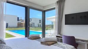 A modern hotel room with a large bed, a desk, a chair, and a TV. There is a pool visible through the windows. - Stunning private villa for 20 guests with WIFI, pool, A/C, TV, terrace and pets allowed (Umag)