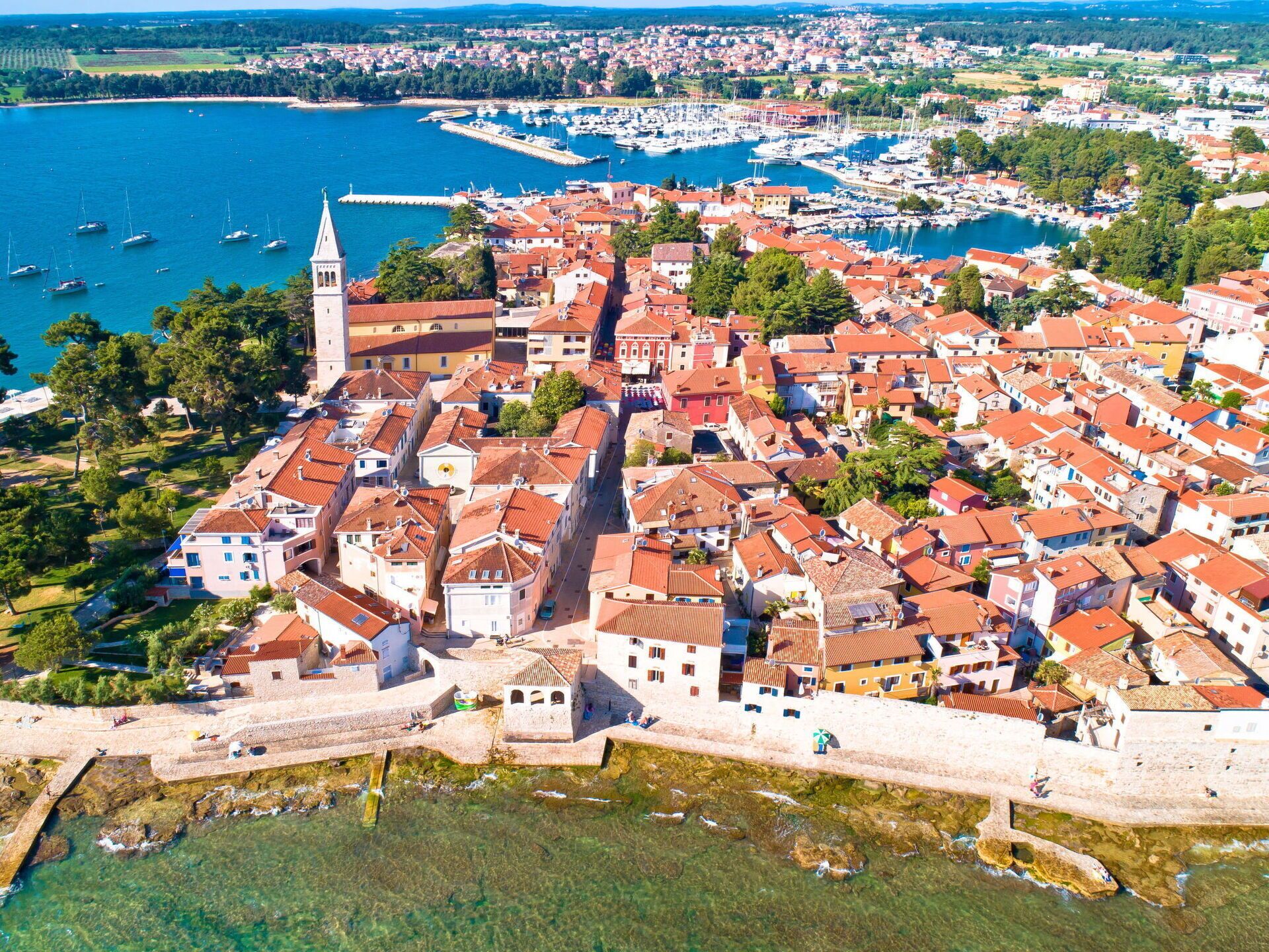 An aerial view of a coastal town with historic buildings, a prominent church tower, and a marina.