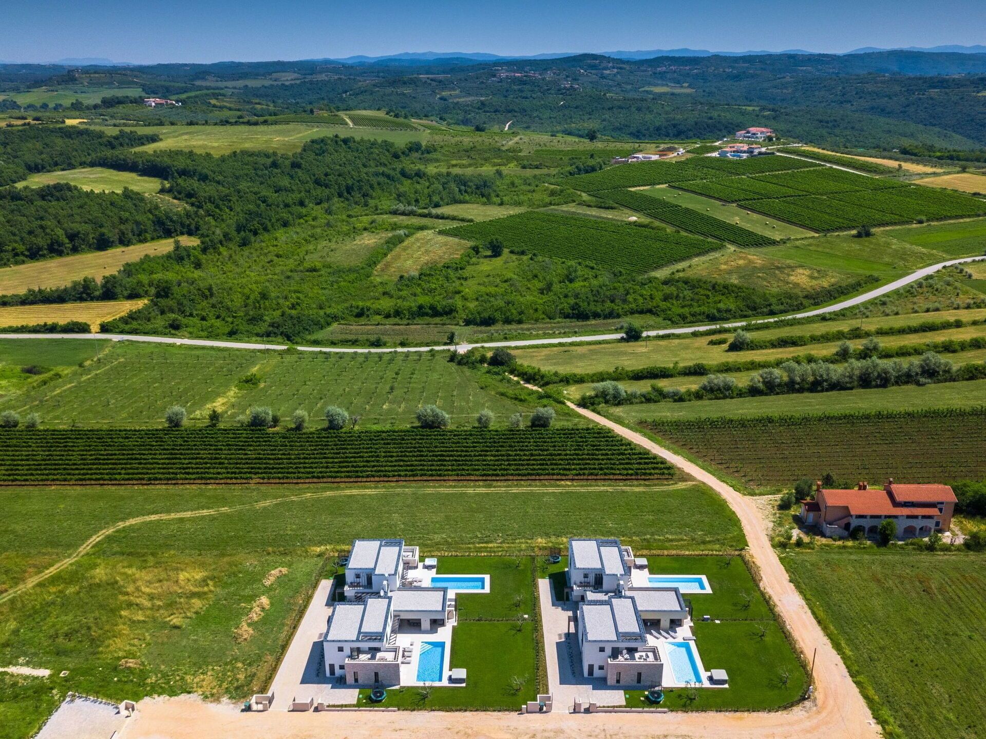 An aerial view of a vineyard with two modern buildings, a swimming pool, and a dirt road.
