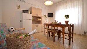 Una sala de estar acogedora con sofá, una mesa de comedor con sillas, televisión y una zona de cocina con armarios y microondas.