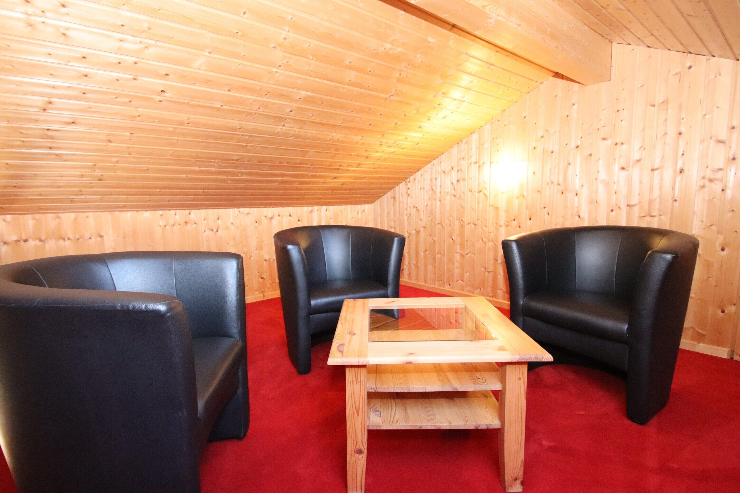 A room with wooden walls and a sloped ceiling, featuring two black leather chairs and a wooden table.