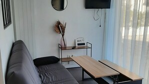A modern living room with a sofa, a coffee table, a TV, and a small table with a vase and a Wi-Fi password sign. - Pti'Bonheur, apartment 4 pers (Toulouse)